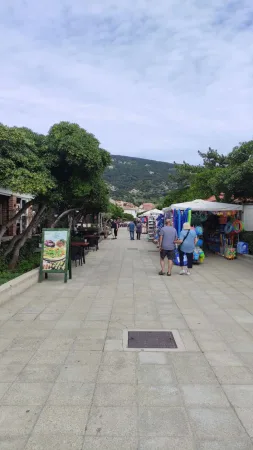 Rušná promenáda v Bašce s obchůdky, turisty a výhledem na kopce