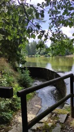 Kamenný jez na rybníku s dřevěným zábradlím a schůdky