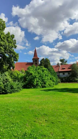 Kostelní věž vyčnívající nad zelení Průhonického parku