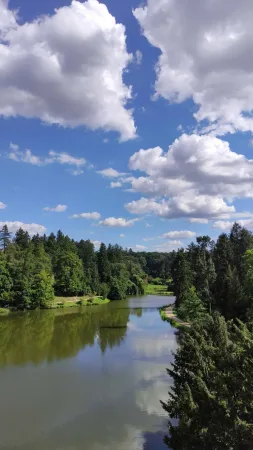 Řeka protékající parkem pod oblačnou oblohou