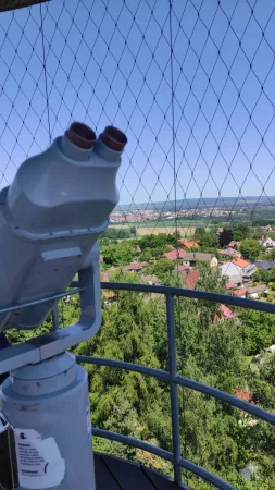 Dalekohled na rozhledně Hýlačka s výhledem na střechy domů a krajinu