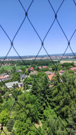 Pohled z rozhledny Hýlačka přes ochrannou ocelovou síť na vesnici a krajinu