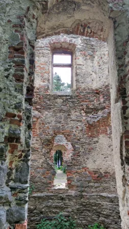 Pohled skrz kamenné a cihlové zdi zříceniny Belveder na okenní otvor s výhledem na stromy