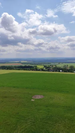 Zelené pole a vesnice v dálce při pohledu z vyhlídkové plošiny rozhledny Vysoká pod mraky