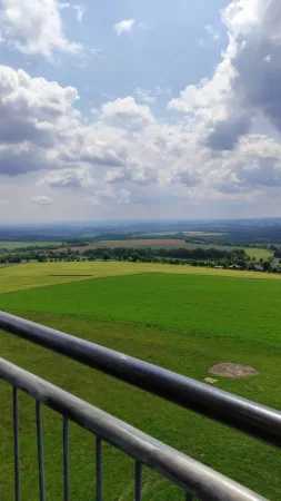 Výhled z rozhledny Vysoká přes zábradlí na zelené pole a krajinu pod mraky