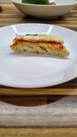 Boční řez špaldovou pizzou na bílém talíři ukazuje kypré těsto, kečup, šunku a sýr