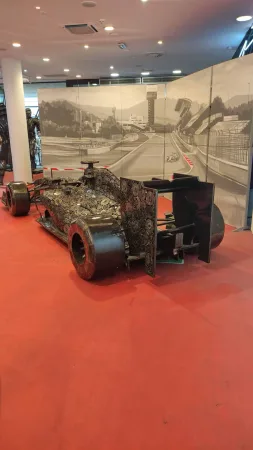 Kovová socha závodního vozu formule 1 s malovanou tratí v pozadí.