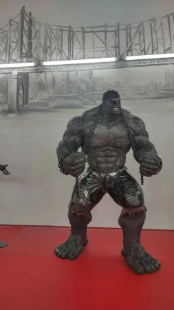 Kovová socha Hulka spoutaného řetězy před malovaným mostem.