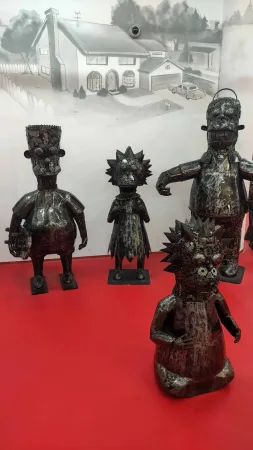 Kovové sochy rodiny Simpsonových před malovaným domem na zdi.