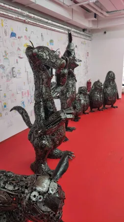 Řada kovových soch zvířat na červené podlaze u nástěnky s dětskými kresbami.
