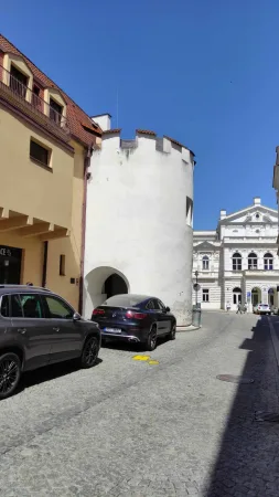 Bílá hradební věž s cimbuřím v úzké uličce Tábora s výhledem na divadlo v pozadí