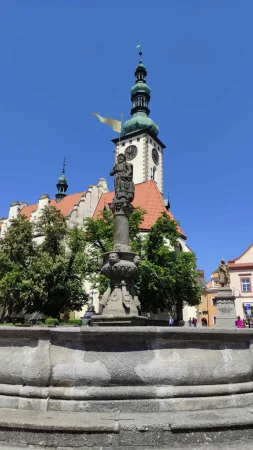 Kamenná kašna se sochou před kostelem se zelenou věží na Žižkově náměstí v Táboře