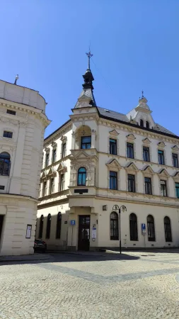 Nárožní měšťanský dům s věžičkou a štuky na dlážděném náměstí v Táboře pod modrou oblohou