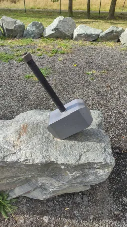 Detailní záběr na rukojeť kovové repliky Thorova kladiva na kameni