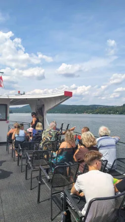 Cestující sedí na palubě výletní lodi a kochají se pohledem na přehradu a okolí.