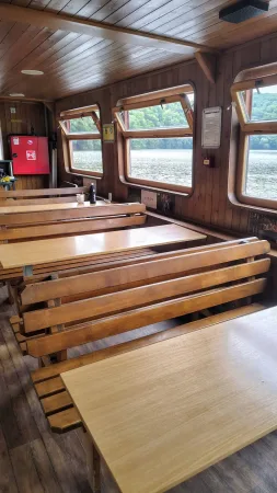 Dřevěné sezení v podpalubí lodi s výhledem na jezero z oken.