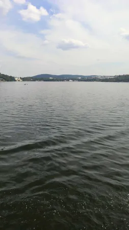 Klidná hladina Brněnské přehrady s výhledem na okolní kopce a městskou zástavbu.