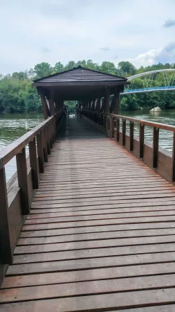 Kryté dřevěné molo vede k vodě s výhledem na obloukový most.