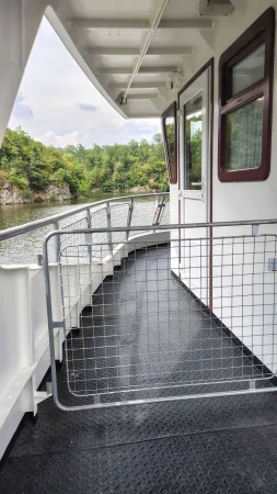 Boční palubní chodba lodi s výhledem na zalesněné kopce kolem přehrady.