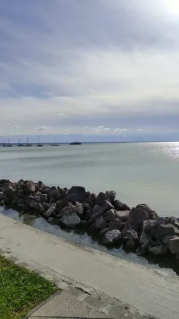 Kamenný vlnolam u břehu Balatonu s plachetnicemi v dáli