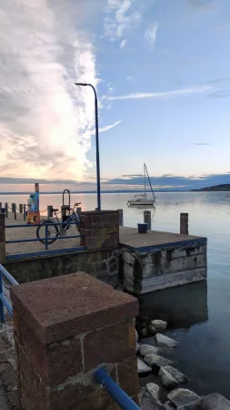 Kolo opřené u přístaviště s plachetnicí na klidném Balatonu
