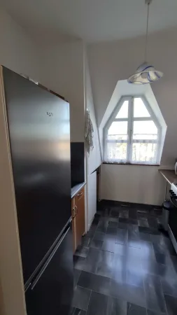 Úzká kuchyně apartmánu s velkou nerezovou lednicí a oknem