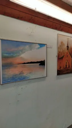 Dva obrazy na výstavě zobrazující západ slunce nad jezerem a kostel