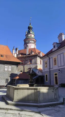 Kamenná kašna na nádvoří s výhledem na barevnou zámeckou věž Českého Krumlova