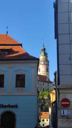 Modrá budova banky v uličce s výhledem na zámeckou věž Krumlova