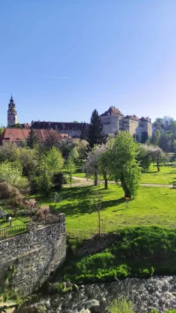 Zámek a město Český Krumlov viděné přes zelený trávník s kvetoucími stromy