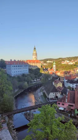Zlatavé večerní světlo nad věží zámku, řekou Vltavou a lávkou v Českém Krumlově