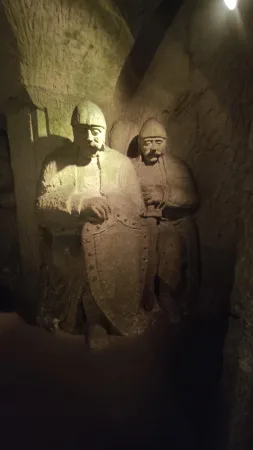 Dvě kamenné sochy rytířů se štíty osvětlené ve tmě jeskyně