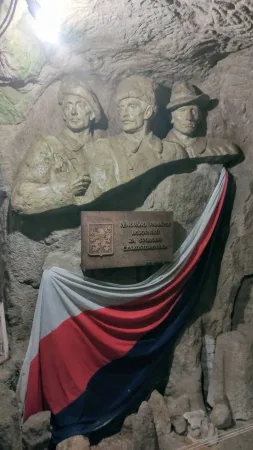 Kamenný reliéf tří legionářů s pamětní deskou a československou vlajkou