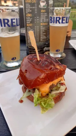 Šťavnatý burger a dvě sklenice nealkoholického piva na stole restaurační zahrádky