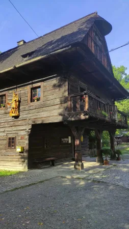 Patrová dřevěná usedlost se sochou a květinovou výzdobou ve skanzenu