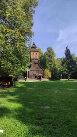 Vysoká dřevěná zvonice s křížem uprostřed zeleného parku ve skanzenu
