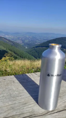 Turistická lahev na dřevěném stole s výhledem do beskydského údolí