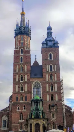 Dvě různě vysoké věže Mariánského kostela v Krakově při pohledu zdola proti zatažené obloze