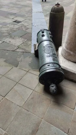 Historické bronzové dělo ležící na dlažbě u kamenného sloupu na nádvoří Collegium Maius v Krakově