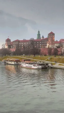 Hrad Wawel nad řekou Vislou v Krakově za soumraku, u břehu kotví vyhlídkové lodě v růžovém světle