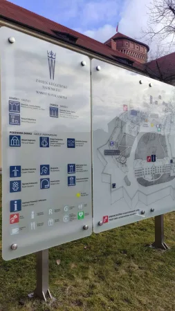 Skleněná informační tabule s plánem hradu Wawel v Krakově, v pozadí cihlová hradní věž