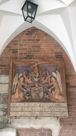 Kamenný reliéf se znakem a dvěma anděly pod gotickou klenbou v podloubí Collegium Maius v Krakově
