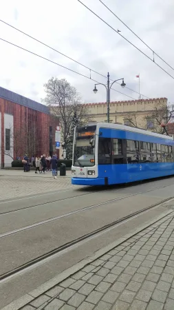Modrá krakovská tramvaj projíždí kolem cimbuří městských hradeb v historickém centru Krakova