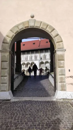Silueta rodiny procházející klenutou branou na renesanční nádvoří hradu Wawel v Krakově