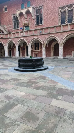 Kamenná studna uprostřed gotického nádvoří Collegium Maius s cihlovými arkádami v Krakově