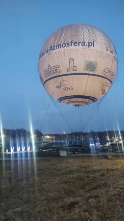 Upoutaný vyhlídkový balón u řeky Visly v Krakově za modré hodinky, na plášti siluety krakovských památek