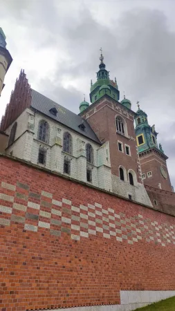 Věže Wawelské katedrály se zelenými kupolemi vystupují nad mohutnou cihlovou hradbou hradu v Krakově