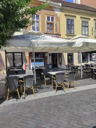 Nyári kávézó terasz fehér napernyőkkel a kövezett soproni téren