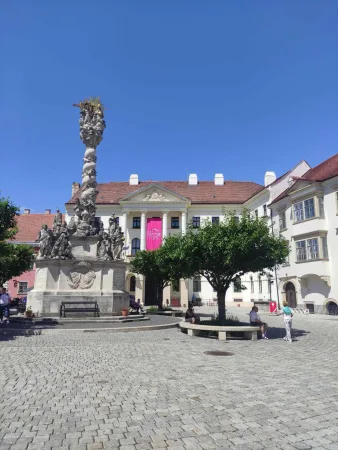 Barokk Mária-oszlop pink bannerrel díszített épülettel a soproni téren