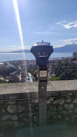 Vyhlídkový dalekohled na hradbách s panoramatem přístavu a moře v pozadí